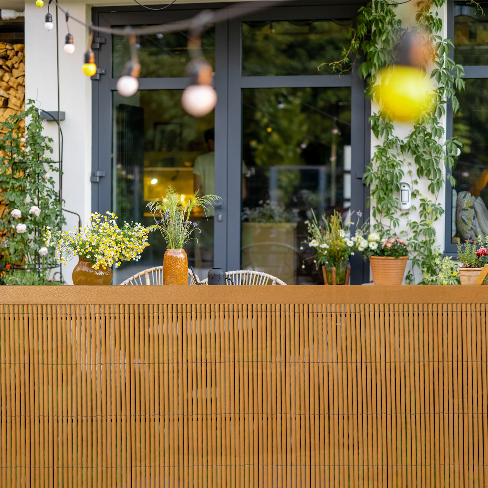 Abdeckprofil für Sichtschutzmatte vor Terrasse mit Pflanzen und Lichterkette