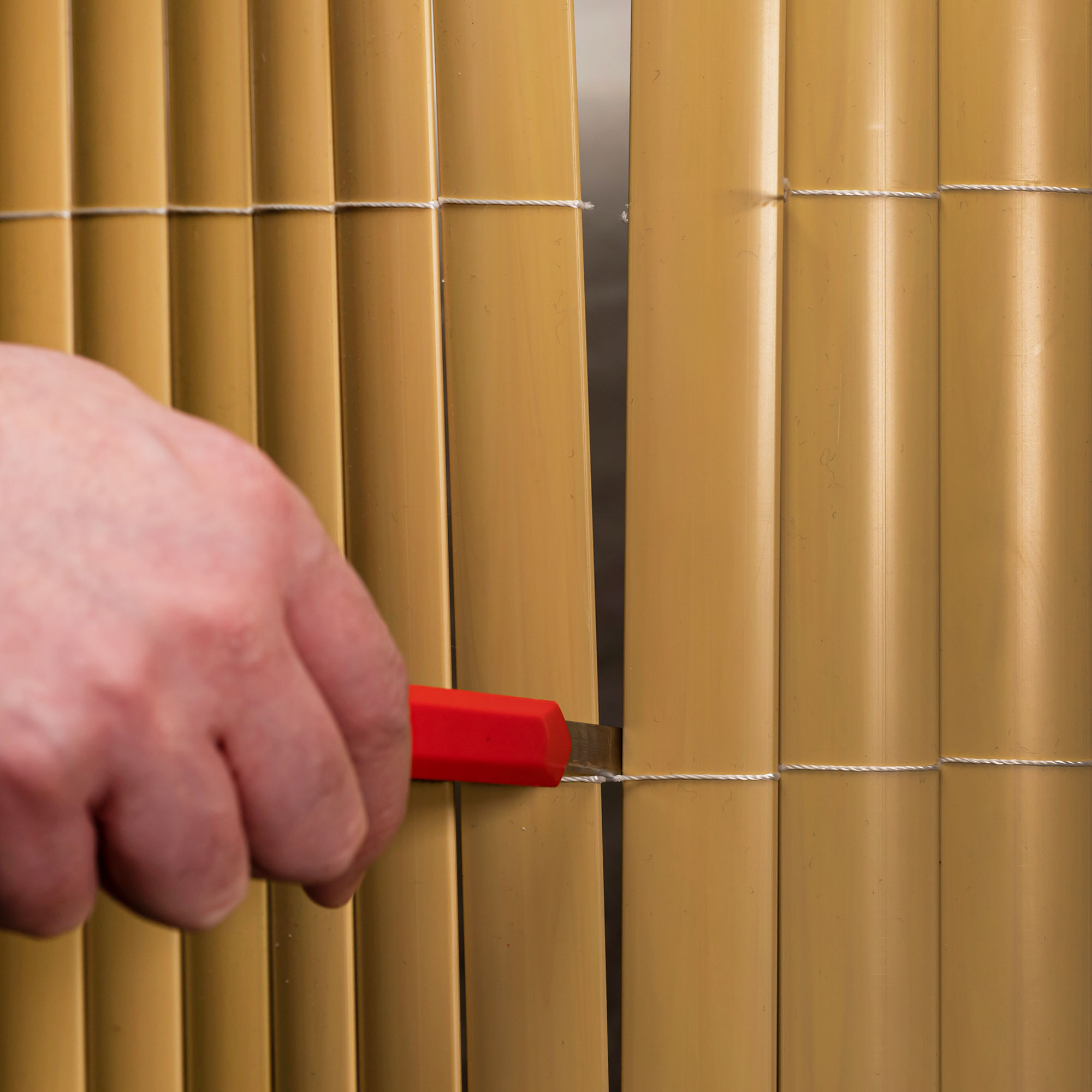 Hand schneidet PVC Sichtschutzmatte mit Messer, zeigt Montage oder Anpassung des Materials