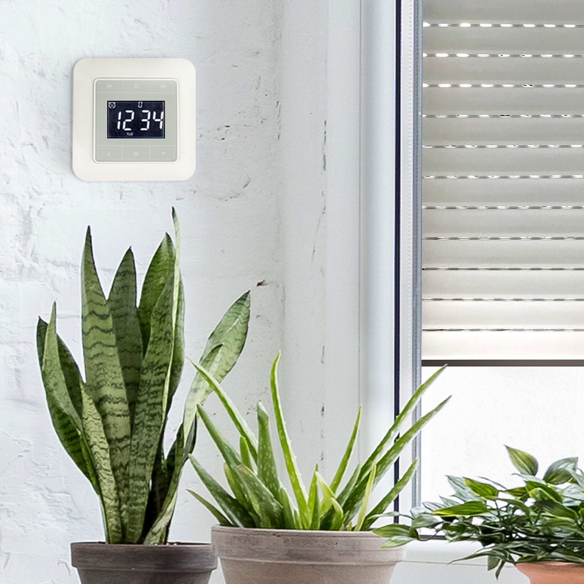 Zeitschaltuhr mit Touch-Display an der Wand neben Pflanzen und einem Fenster mit Jalousie