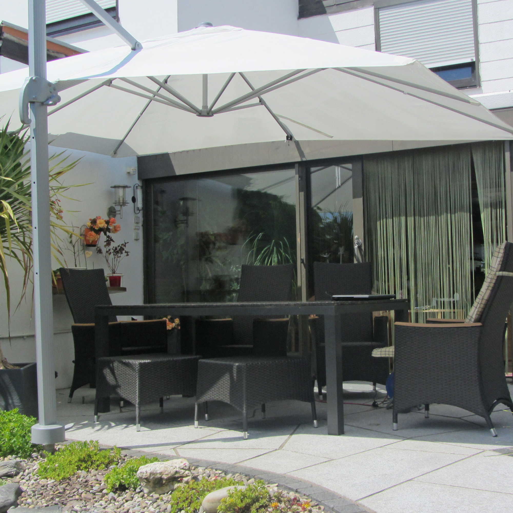 Terrasse mit Ampelschirm über Esstisch und Stühlen, umgeben von Pflanzen und Glasfront