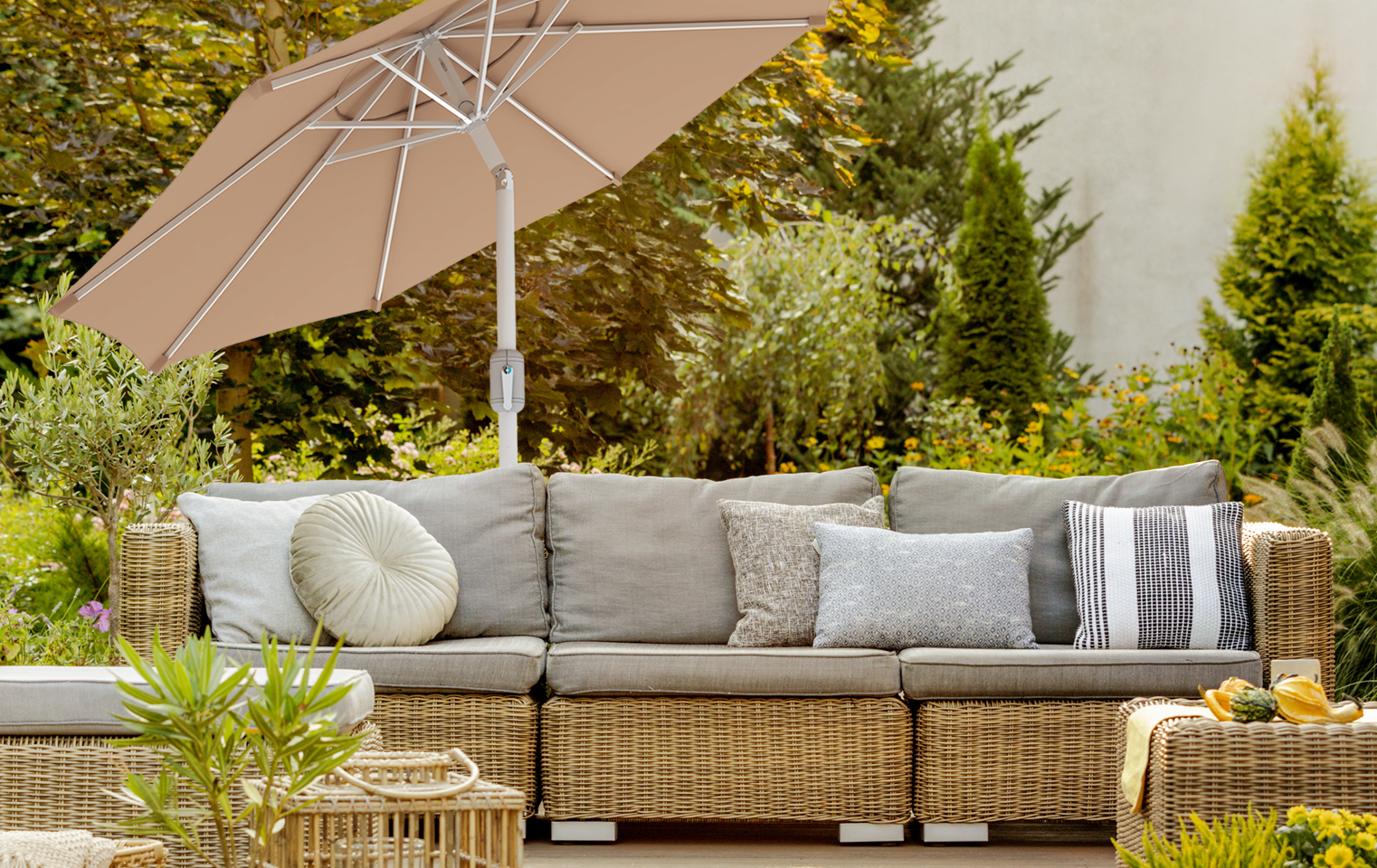 Terrasse mit Rattan-Sofa und interpara Sonnenschirm im Gartenumfeld