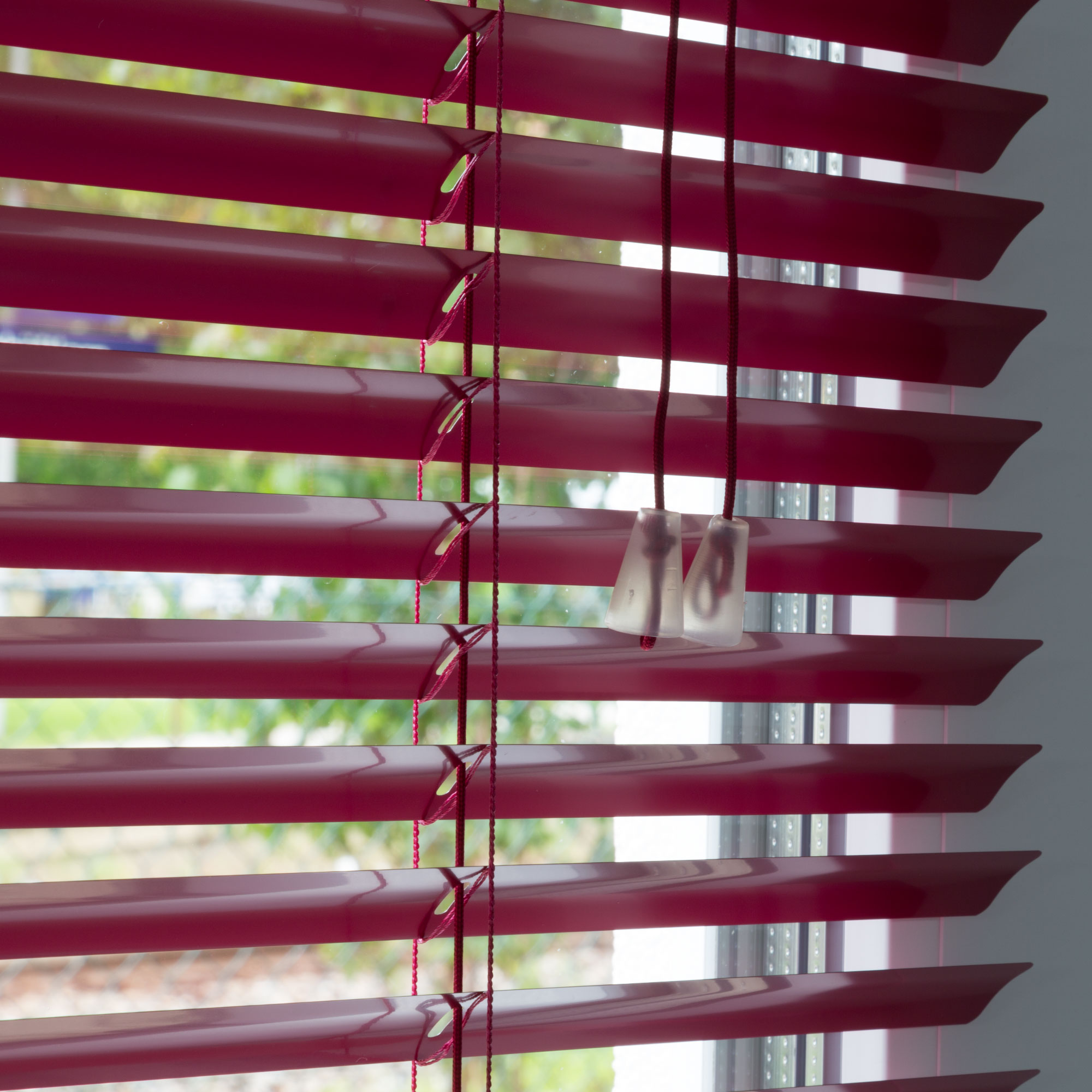Aluminium Jalousie mit Lamellen und Zugkordel vor einem Fenster