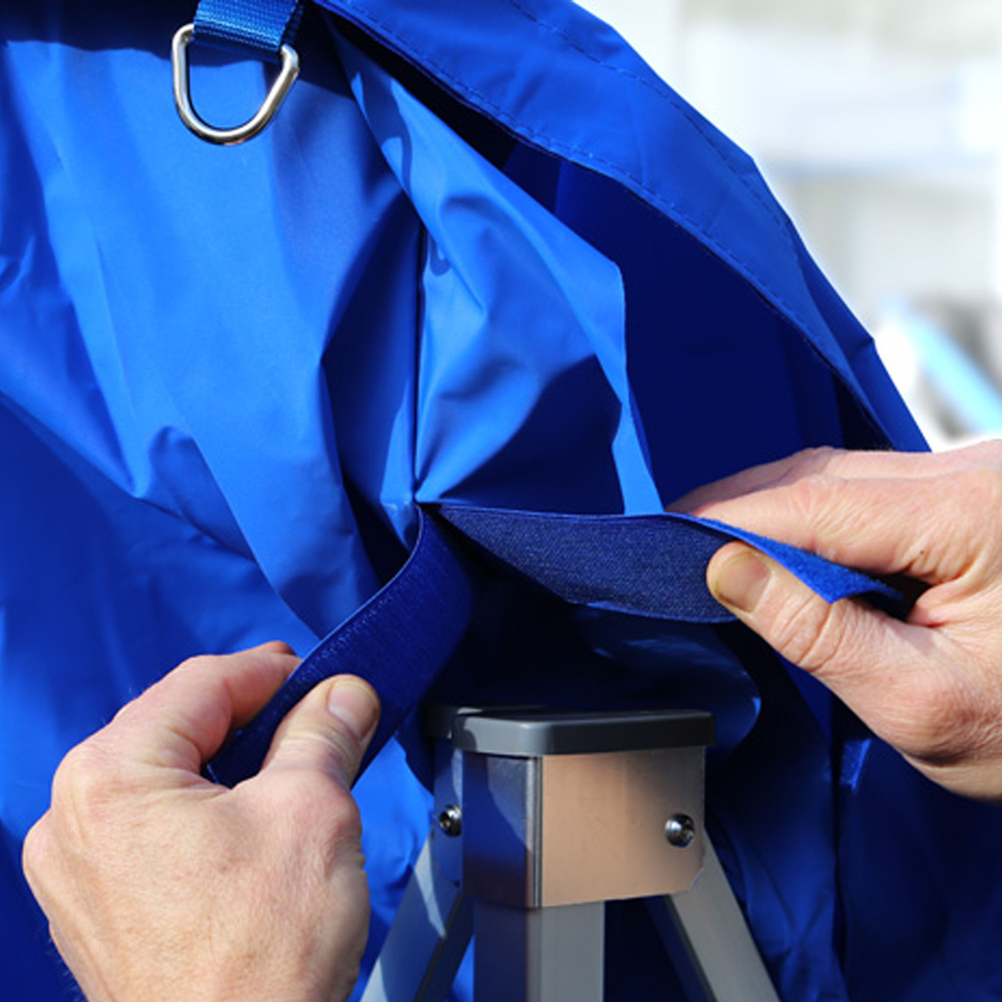 Person befestigt Dach an Faltpavillon mit Klettverschluss und Metallring