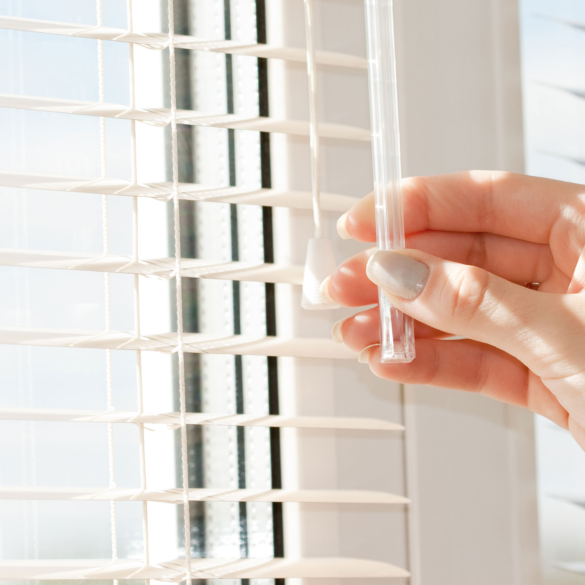 Hand dreht Acryl-Wendestab an Aluminium-Jalousie vor einem Fenster