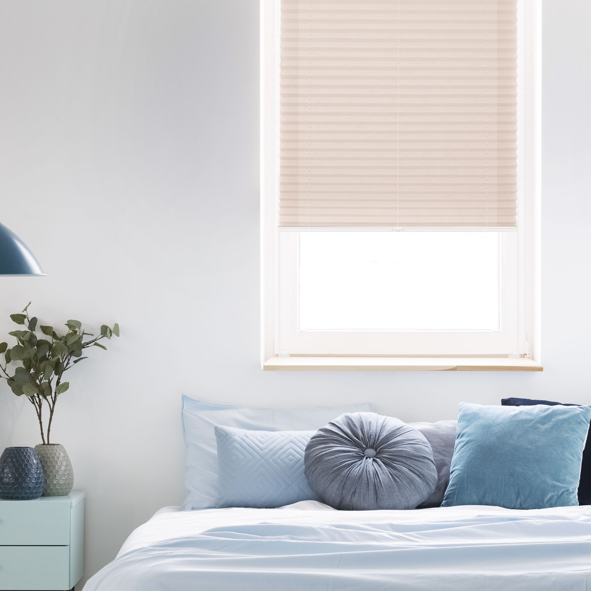 Fenster mit heruntergelassenem Rollo, Bett mit Kissen, Nachttisch mit Vasen und Pflanze