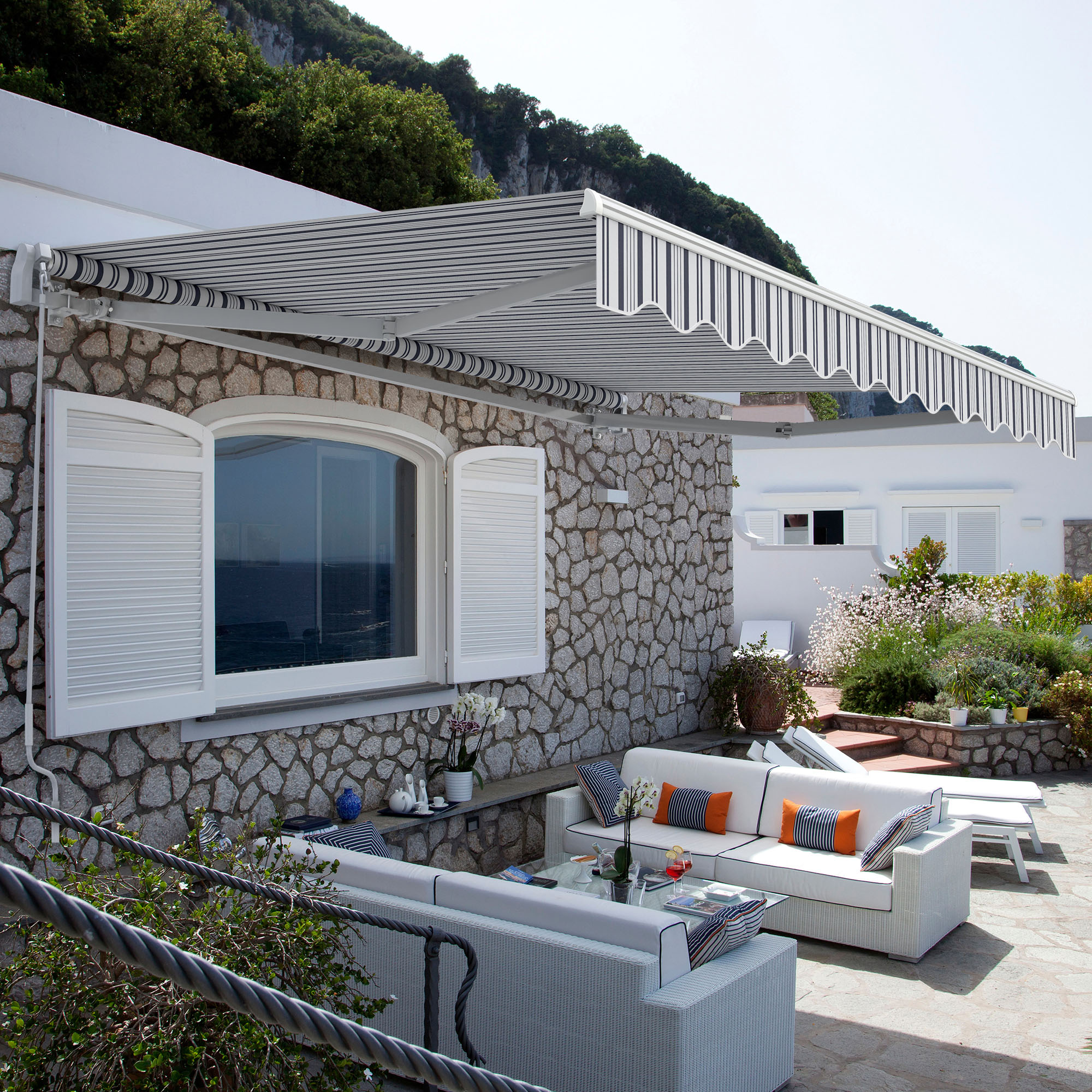 Markise über Terrasse mit Sitzbereich und Pflanzen, montiert an einer Steinwand eines Hauses