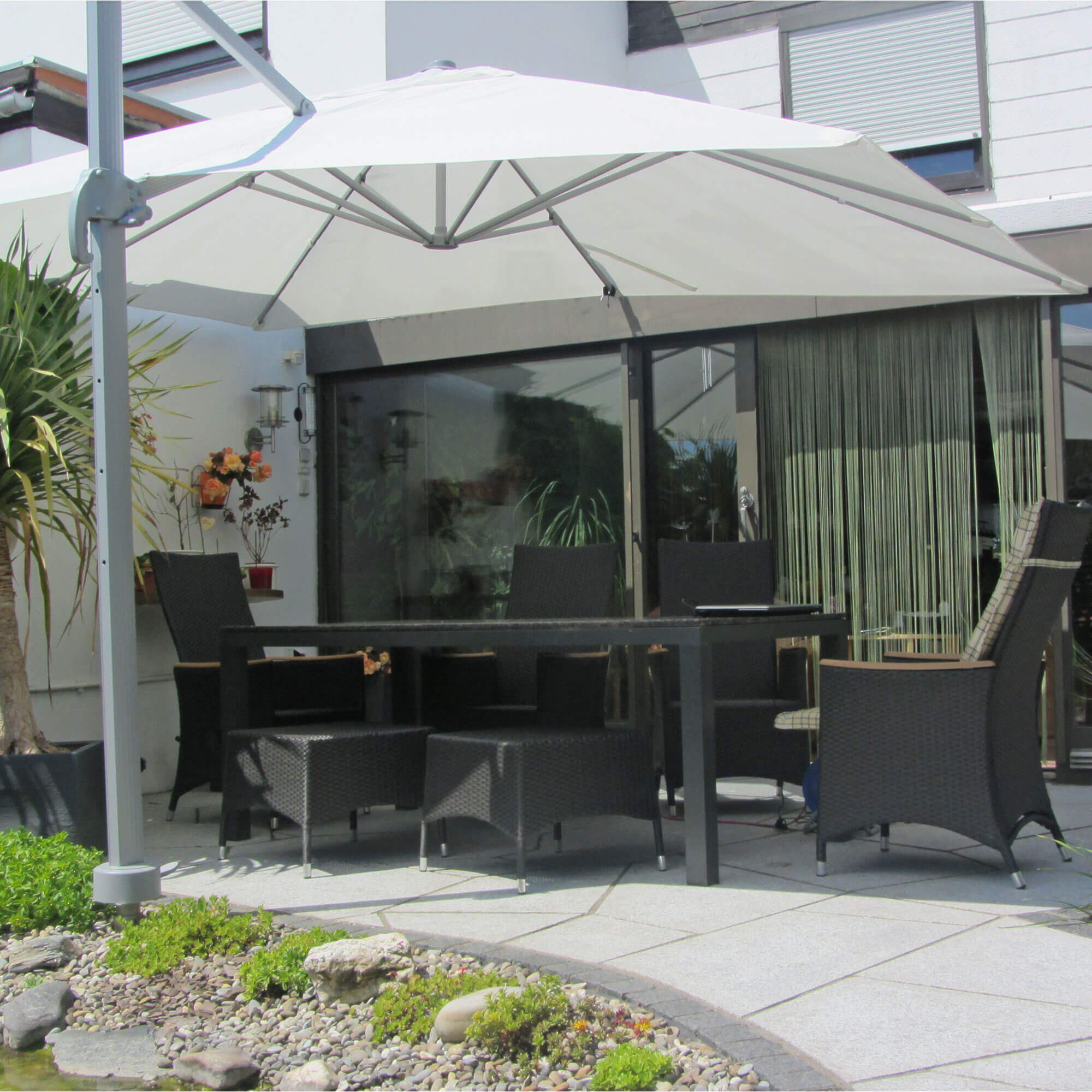 Terrasse mit Ampelschirm und Gartenmöbeln, umgeben von Pflanzen und einem kleinen Teich